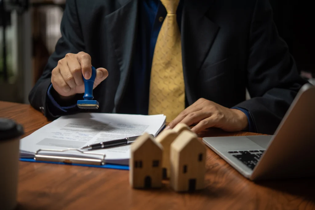 Professional stamping paperwork beside a laptop and model houses