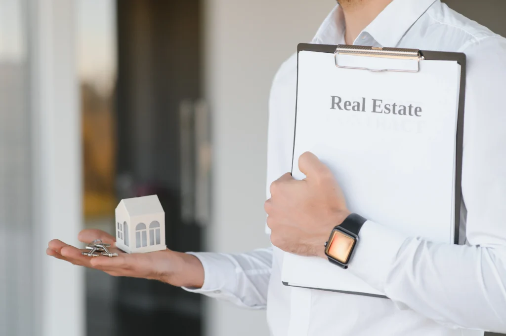 Person holding a real estate clipboard, keys and a model house