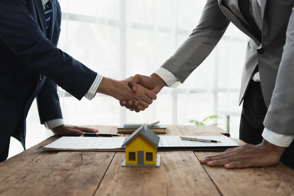 Two professionals shaking hands over real estate documents