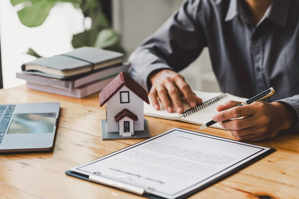 Person reviewing paperwork beside a notebook and model house
